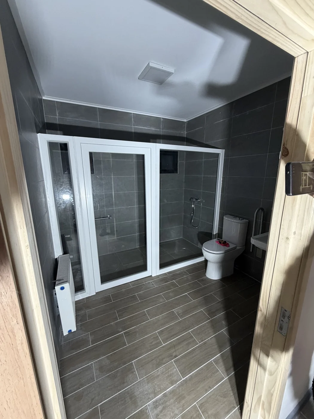 Cerramiento acristalado de ducha con perfiles blancos en un baño de revestimientos grises